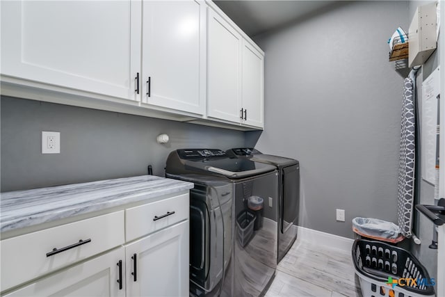 laundry room with cabinets, washing machine and dryer, and light hardwood / wood-style flooring