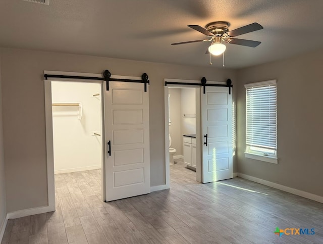 unfurnished bedroom with a spacious closet, a barn door, a textured ceiling, and light wood-type flooring