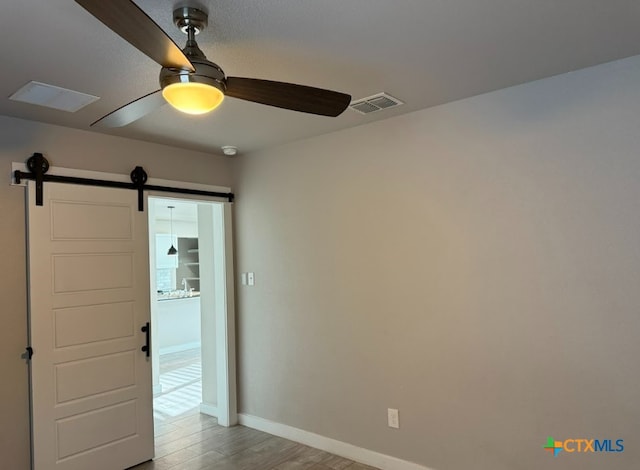 spare room featuring ceiling fan, a barn door, and light hardwood / wood-style floors