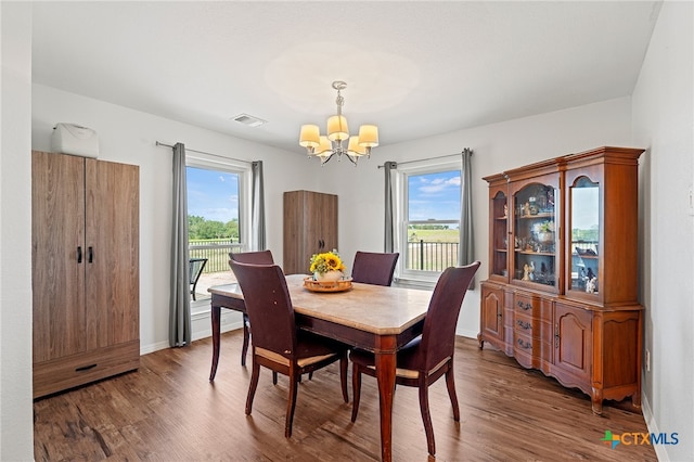 dining area with plenty of natural light, dark hardwood / wood-style floors, and an inviting chandelier