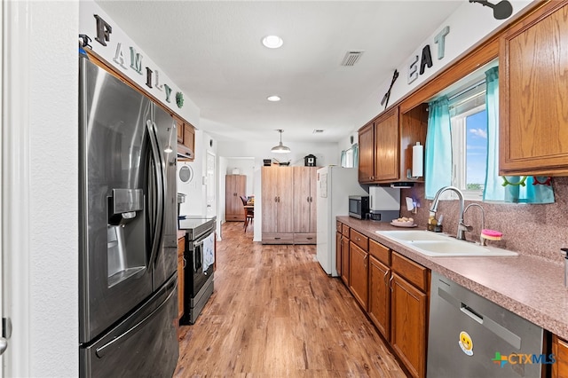 kitchen with sink, appliances with stainless steel finishes, tasteful backsplash, decorative light fixtures, and light wood-type flooring