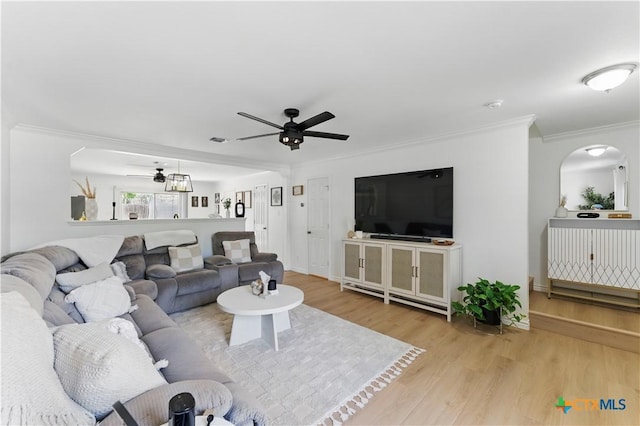 living room featuring arched walkways, baseboards, wood finished floors, ceiling fan, and ornamental molding