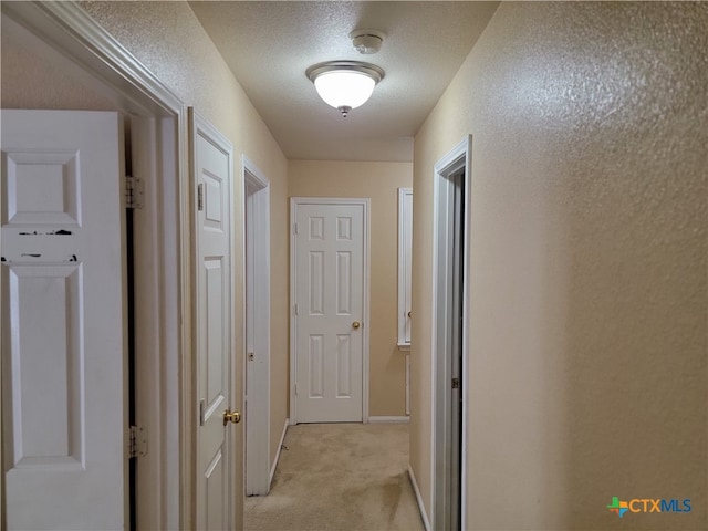 corridor featuring a textured ceiling and light carpet