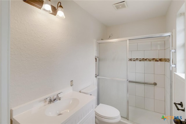 bathroom featuring toilet, a stall shower, visible vents, a textured wall, and vanity