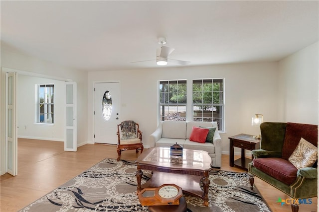 living area featuring light wood finished floors, baseboards, ceiling fan, and plenty of natural light