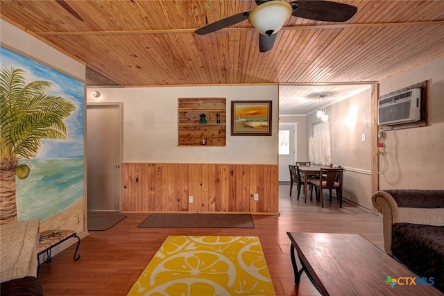 living room with ceiling fan, a wainscoted wall, wood ceiling, a wall unit AC, and wood finished floors