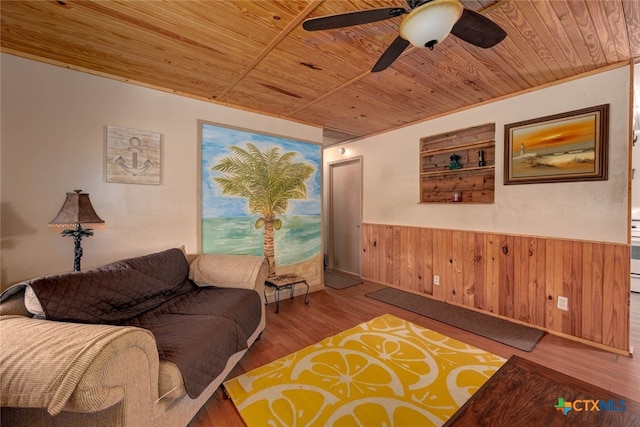 living area with a wainscoted wall, wood walls, wood ceiling, wood finished floors, and a ceiling fan