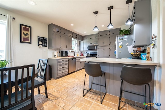 kitchen featuring sink, kitchen peninsula, decorative light fixtures, gray cabinets, and appliances with stainless steel finishes