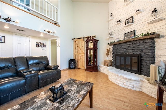 living room featuring a barn door, wood-type flooring, a fireplace, and a high ceiling