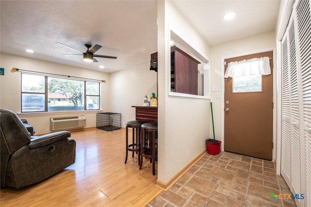 foyer entrance featuring ceiling fan, light wood-type flooring, an AC wall unit, and a textured ceiling