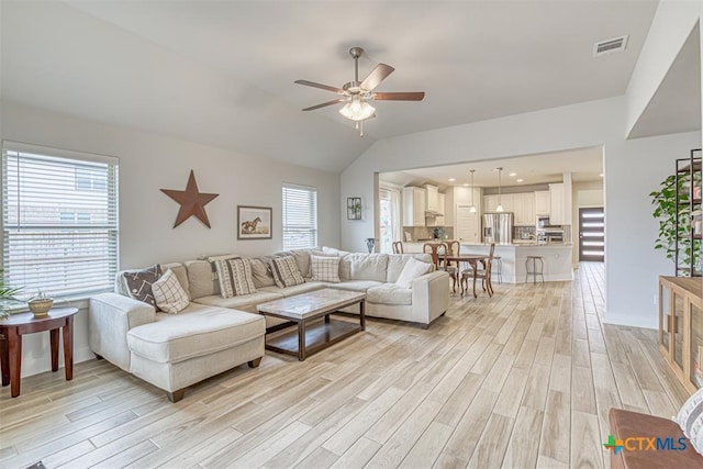 living area with lofted ceiling, ceiling fan, light wood-style floors, and a healthy amount of sunlight