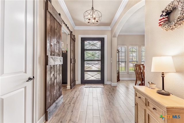 entrance foyer with ornamental molding, light wood-type flooring, a barn door, and a chandelier