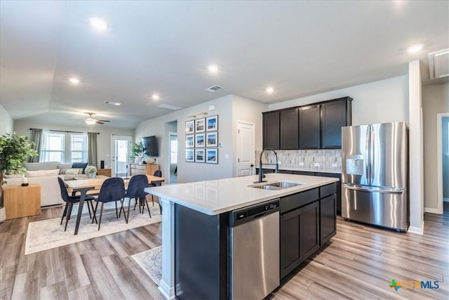 kitchen featuring light countertops, decorative backsplash, appliances with stainless steel finishes, a sink, and an island with sink