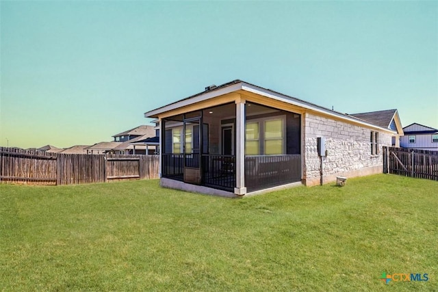 back of property featuring stone siding, a sunroom, a fenced backyard, and a yard