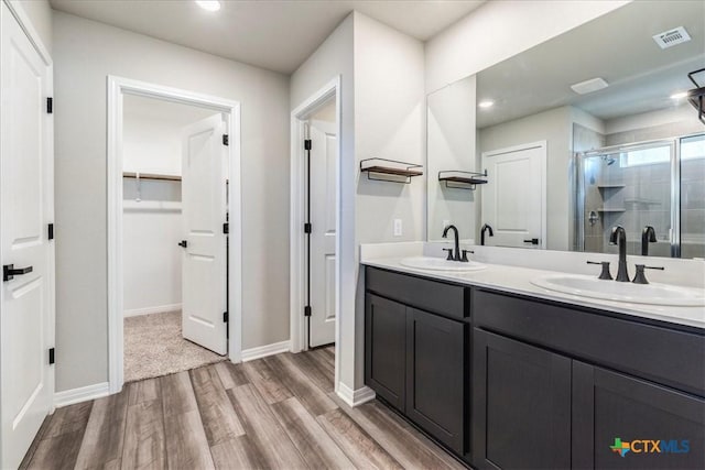 full bath featuring a stall shower, double vanity, a sink, and wood finished floors