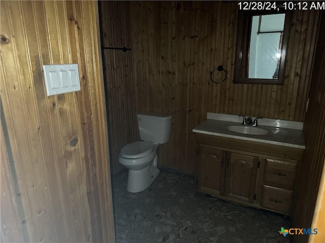 bathroom featuring toilet, vanity, and wood walls