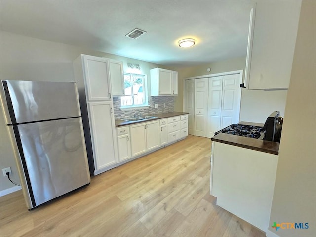 kitchen with white cabinets, sink, decorative backsplash, stainless steel fridge, and light wood-type flooring