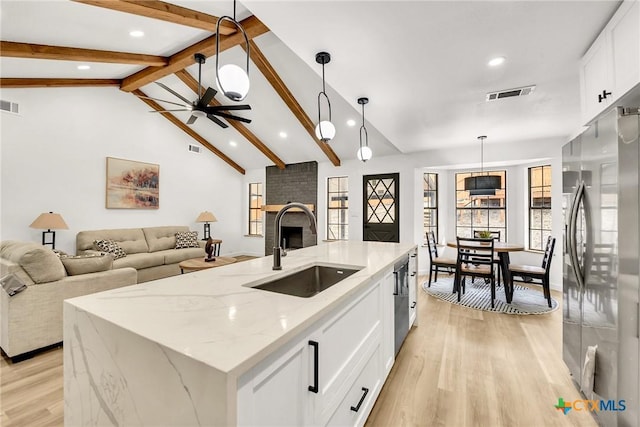 kitchen featuring pendant lighting, stainless steel fridge, light stone countertops, an island with sink, and white cabinets