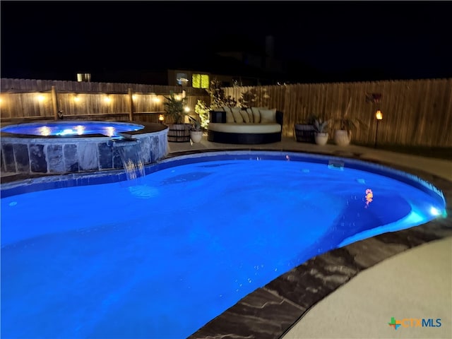 pool at twilight featuring pool water feature and an in ground hot tub