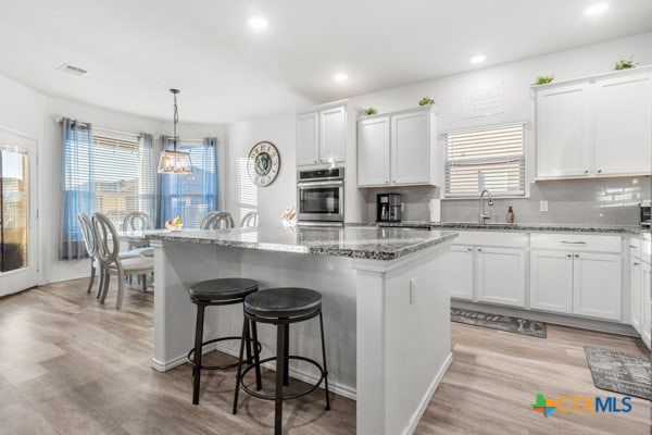 kitchen with stainless steel oven, pendant lighting, a center island, light wood-type flooring, and white cabinetry