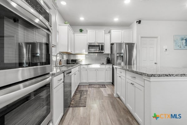 kitchen with light stone countertops, light hardwood / wood-style flooring, white cabinets, appliances with stainless steel finishes, and sink