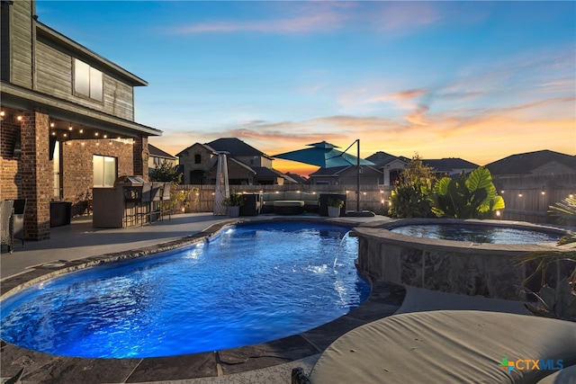 pool at dusk with a patio area, exterior bar, and an in ground hot tub