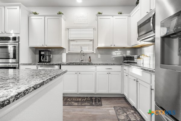 kitchen featuring light stone counters, stainless steel appliances, dark hardwood / wood-style flooring, white cabinetry, and sink