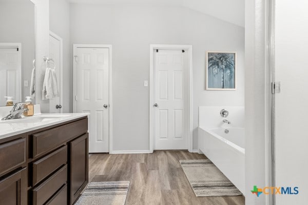 bathroom with hardwood / wood-style floors, a tub, vaulted ceiling, and vanity