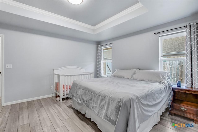 bedroom featuring wood finished floors, a tray ceiling, ornamental molding, and baseboards