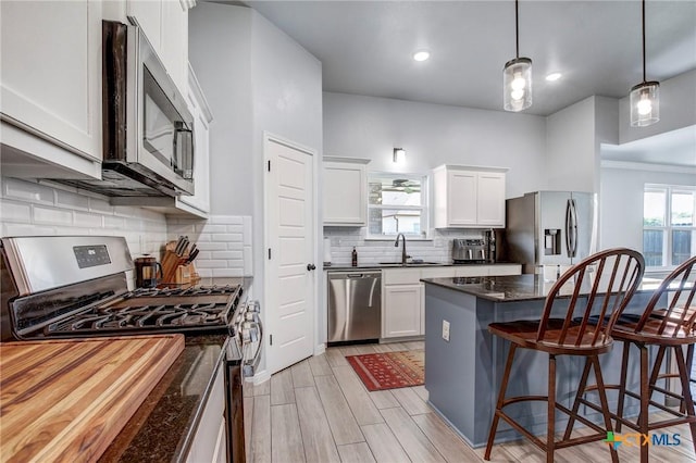 kitchen with a sink, tasteful backsplash, a breakfast bar area, white cabinetry, and appliances with stainless steel finishes
