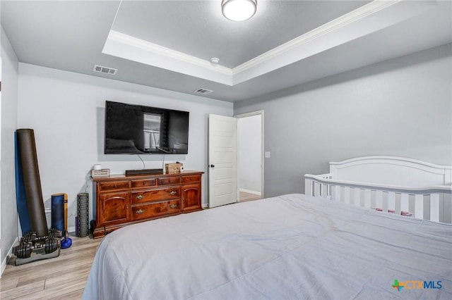 bedroom with wood finished floors, visible vents, crown molding, and a tray ceiling