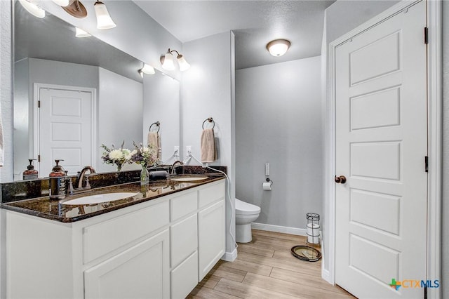 bathroom featuring wood finished floors, toilet, baseboards, and a sink