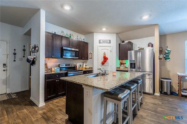 kitchen featuring dark hardwood / wood-style flooring, dark brown cabinetry, stainless steel appliances, a kitchen island with sink, and sink