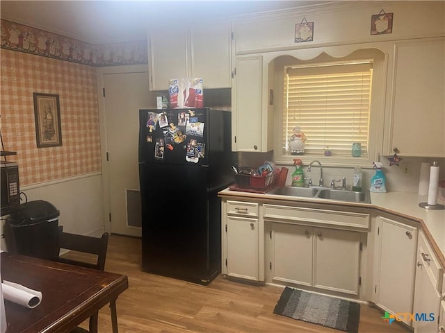 1002 Magnolia St, Belton, TX 76513 - kitchen featuring freestanding refrigerator, a sink, white cabinetry, light wood-style floors, and wallpapered walls