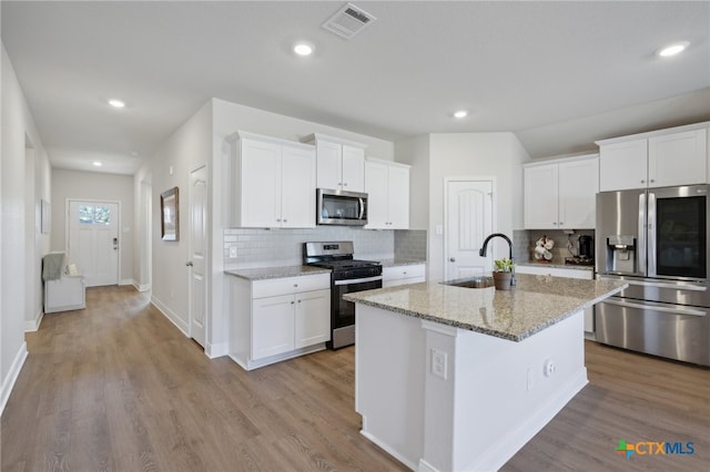 kitchen with stainless steel appliances, sink, light hardwood / wood-style floors, white cabinetry, and an island with sink