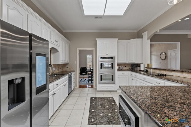 kitchen featuring appliances with stainless steel finishes, white cabinets, a sink, light tile patterned flooring, and dark stone countertops