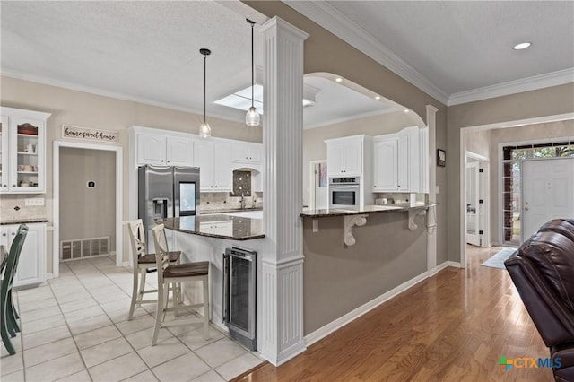 kitchen with a breakfast bar area, visible vents, appliances with stainless steel finishes, white cabinets, and beverage cooler