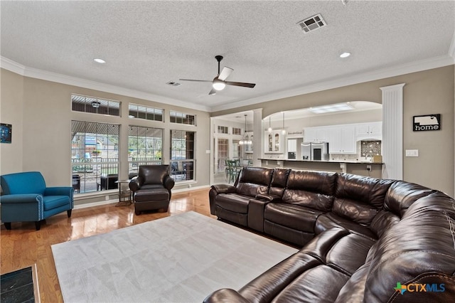 living area with visible vents, ceiling fan, wood finished floors, crown molding, and a textured ceiling