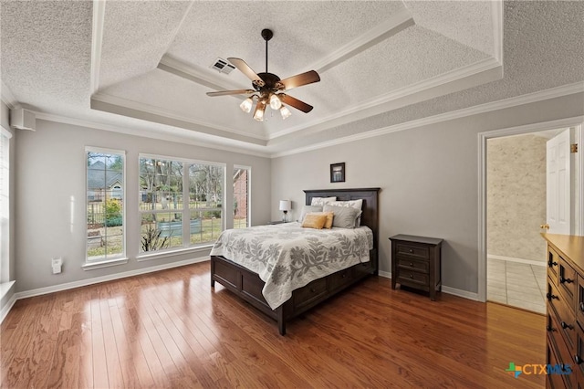 bedroom with a textured ceiling, hardwood / wood-style flooring, visible vents, ornamental molding, and a raised ceiling