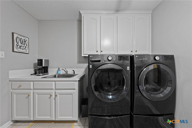 clothes washing area with cabinet space, light tile patterned floors, a textured ceiling, washing machine and dryer, and a sink