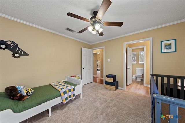 carpeted bedroom with crown molding, visible vents, ensuite bathroom, a textured ceiling, and baseboards