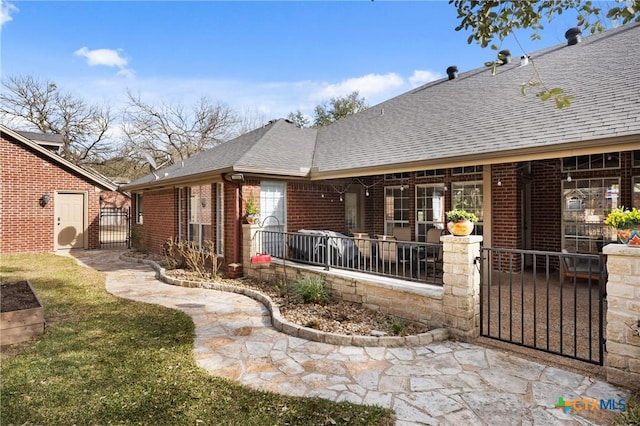 back of house with covered porch, a shingled roof, a gate, and brick siding