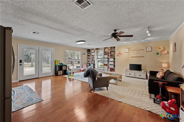 living area with a textured ceiling, wood finished floors, visible vents, and crown molding