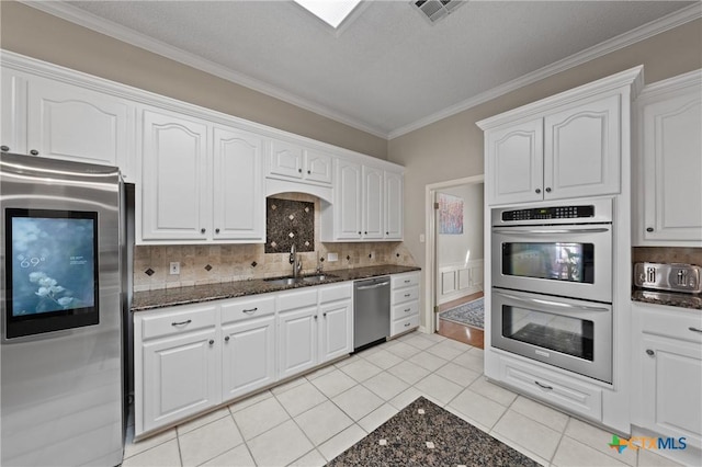 kitchen with visible vents, appliances with stainless steel finishes, dark stone countertops, white cabinetry, and a sink