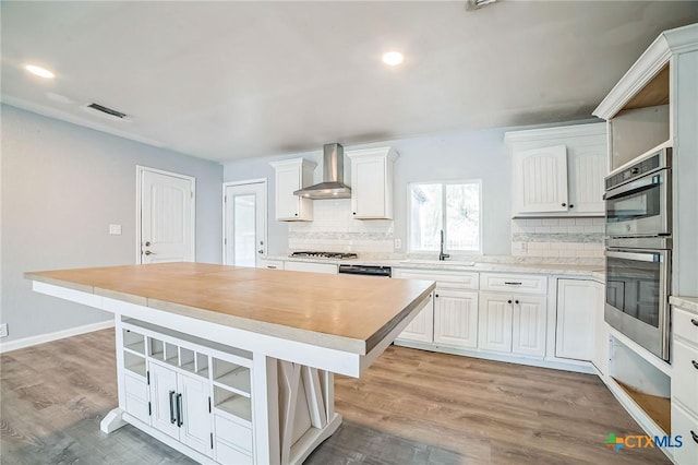 801 E Johnson St, Burnet, TX 78611 - kitchen featuring appliances with stainless steel finishes, tasteful backsplash, wall chimney range hood, a center island, and white cabinets