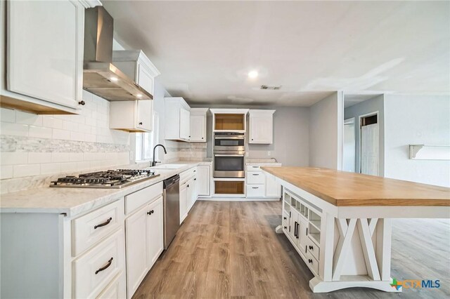 801 E Johnson St, Burnet, TX 78611 - kitchen with stainless steel appliances, wall chimney exhaust hood, light wood-style floors, backsplash, and white cabinets