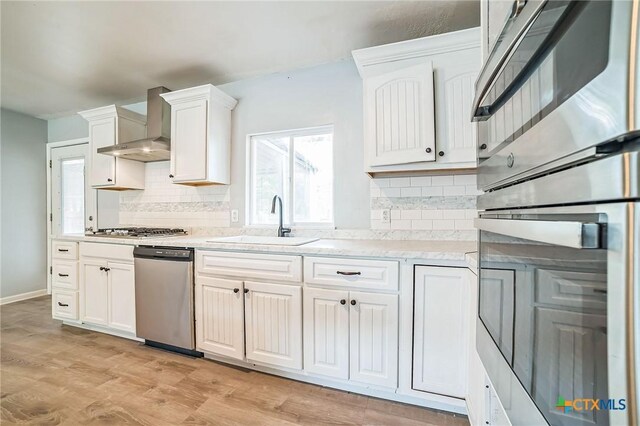 801 E Johnson St, Burnet, TX 78611 - kitchen featuring appliances with stainless steel finishes, a sink, wall chimney exhaust hood, white cabinetry, and backsplash