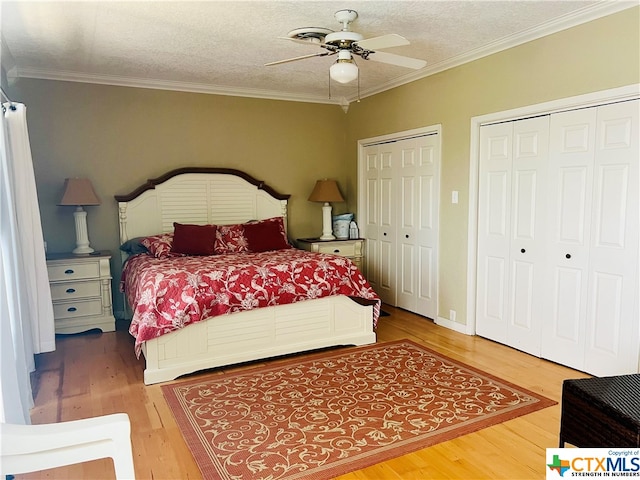 bedroom with wood-type flooring, a textured ceiling, ornamental molding, ceiling fan, and multiple closets