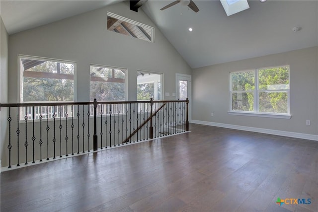 unfurnished room with a healthy amount of sunlight, dark hardwood / wood-style flooring, high vaulted ceiling, and a skylight