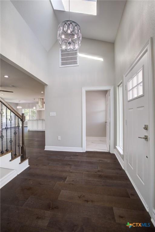 foyer entrance featuring a skylight, high vaulted ceiling, dark wood-type flooring, and a notable chandelier